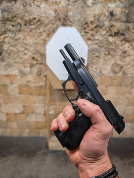 BALTIC STATE &mdash; APRIL 28, 2026: A shooter holds a Beretta 84 semi-automatic pistol in a firing position at an indoor shooting range, showcasing the classic Italian firearm design and handgun safety.