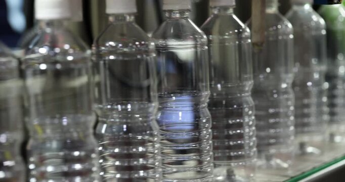 Empty plastic bottles pass through automated bottling line before filling stage. Industrial preparation process for beverage production and packaging workflow.