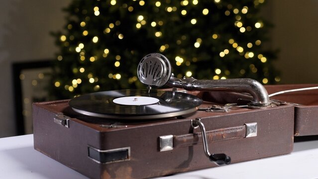 Vintage gramophone with a spinning vinyl record bringing nostalgia and classic music to a festive holiday season, illuminated by a blurred christmas tree background