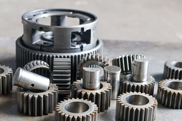 Obraz premium ​A detailed view of a disassembled planetary gear carrier and various steel cogs with spindles on a textured industrial workshop floor.