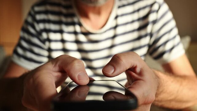 Close-up of a middle-aged man in striped shirt, deeply focused and nervously tapping on his black smartphone. 4K.