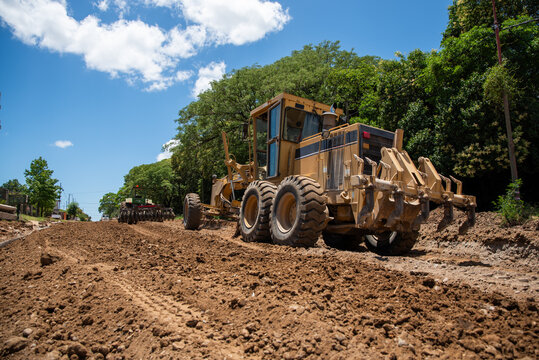 English: Heavy motor grader leveling dirt on a road construction site under a blue sky