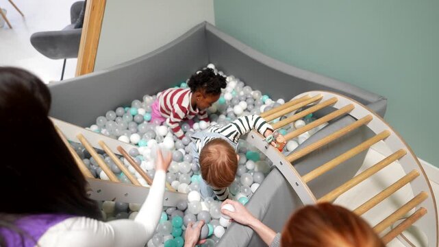 Toddlers playing together in a ball pit at daycare with teachers