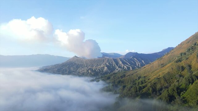 Stunning 4K wide shot of Mount Bromo volcano erupting smoke above a thick sea of clouds at dawn.