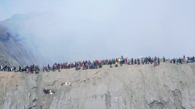 Crowds of tourists walking along the narrow crater rim of Mount Bromo volcano in 4K resolution.
