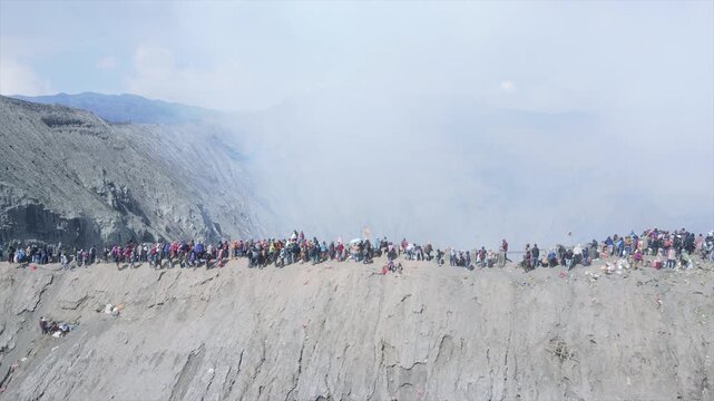 Crowds of tourists walking along the narrow crater rim of Mount Bromo volcano in 4K resolution.