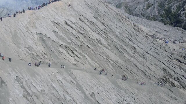 Adventurous tourists hike a narrow, steep volcanic ash path on Mount Bromo's rugged slope.