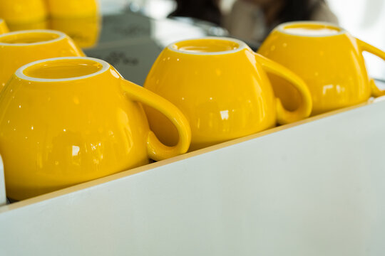 A vibrant and clean yellow ceramic coffee glass lie upside down on a coffee machine in a cafe.