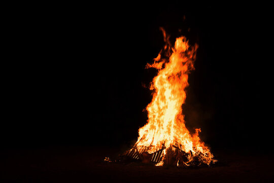 A tall bonfire is lit outdoors at night to celebrate the summer solstice - Līgo