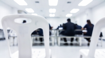 Fototapeta premium Blurred view of people sitting in a classroom or seminar hall with white chairs in the foreground