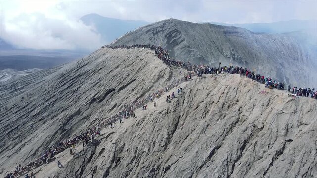 Crowds of people standing on the smoking edge of Mount Bromo active volcano crater in Indonesia.