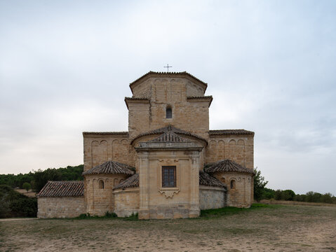 A symmetrical architectural shot of a medieval stone church featuring rounded apses and a central octagonal tower. The limestone structure stands in a rural landscape under a cloudy sky.
