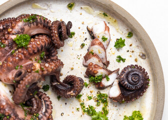 Boiled octopus tentacles and sliced pieces on ceramic plate top view. Olive oil and parsley dressing © katrinshine