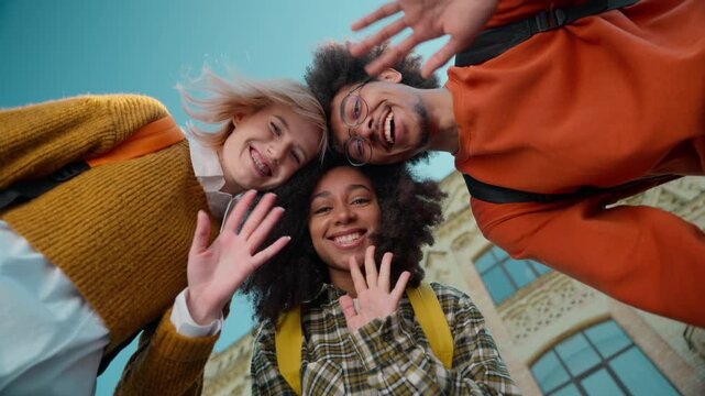 Bottom view happy smiling multiracial students waving hands hello at camera three multiethnic diversity friends African man guy male Caucasian girls women females greeting in city sky outdoor gesture