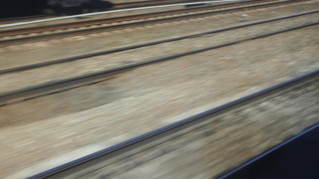 Dynamic motion blur across railway tracks as seen from high-speed train window during daytime journey. Parallel lines of steel rails create sense of rapid movement and forward progress. View captures 