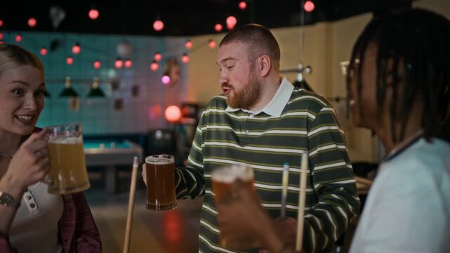 Medium shot of multiethnic group of young adult friends toasting with mugs of beer celebrating good game at billiard hall