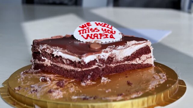 chocolate farewell cake with personalized message on a gold tray inside a bright office. The dessert features cream layers and rich frosting during a goodbye party.