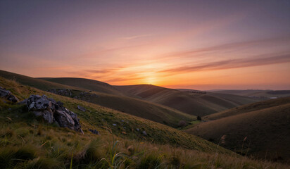 Fototapeta premium Rolling grassy hills under colorful sunset sky in valley