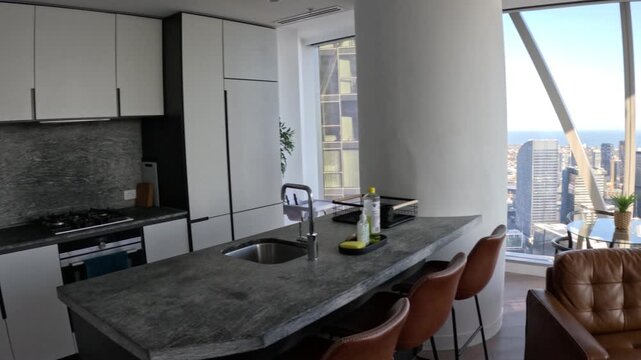 Modern luxury apartment interior pan showing sleek kitchen and scenic city harbor views through large windows.