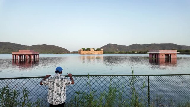 A man stands looking at Jal Mahal palace across Man Sagar Lake.