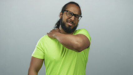 Naklejka premium Man clutching shoulder and wincing while wearing neon green shirt in gray studio after intense workout session; discomfort.