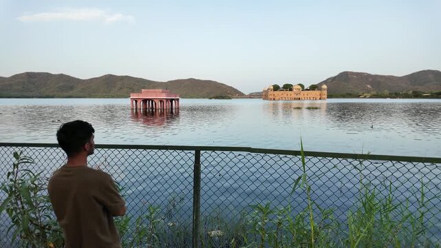 A man stands by a fence observing the historical Jal Mahal palace.