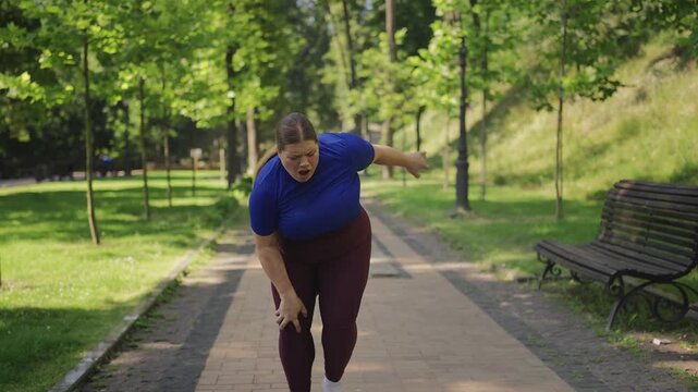 Young plus-size woman jogging in park, suffering sudden knee pain, joint ache