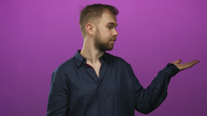 Fototapeta premium Young man showing open palm and raised hand gesture as if presenting an object in a studio with purple backdrop; skepticism.