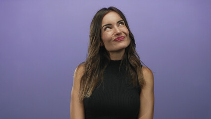 Naklejka premium Woman with wavy brunette hair smiles with pursed lips and tilts head gently in purple studio; playfulness curiosity spontaneity creativity.