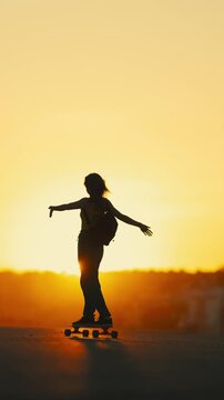 Silhouette of a woman skateboarding at golden sunset
