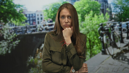 Fototapeta premium Woman hand on chin with folded arm on amsterdam street by canal and bicycles, watch and red bracelet visible; pensive doubt.