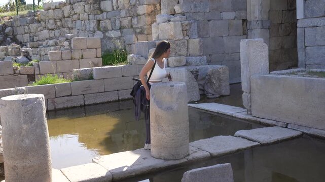 Woman exploring partially flooded ancient ruins of Teos with a smartphone
