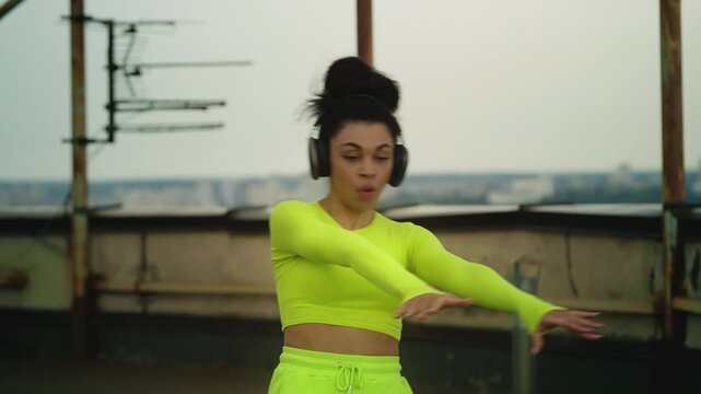 Woman in stylish outfit dancing to music in headset on rooftop, performance