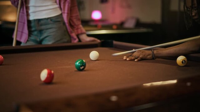 Cropped shot of young adult African American man aligning shot with focus then hitting cue ball during friendly match at pool hall, slow motion