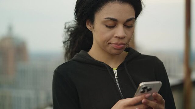 Young Black woman messaging on phone on rooftop, receiving bad news