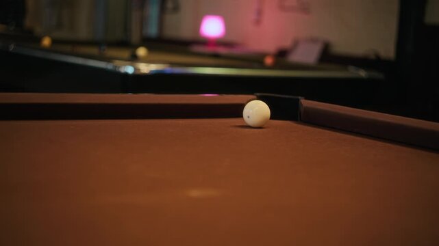 Rack focus shot of unrecognizable man lining up shot on brown felt billiard table then pocketing ball with precision while playing pool in game room, slow motion
