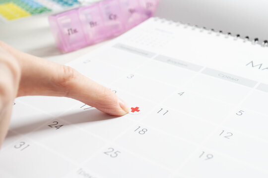 close-up finger presses medical cross sticker on calendar, follow-up appointment planning