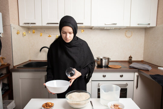 woman holds an empty white bowl and glass beside rice, water and ingredients, preparing the next stage of grain rinsing in a neat home kitchen