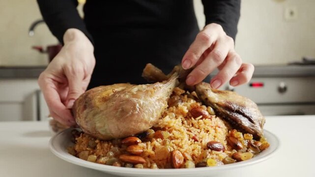 hands placing a roasted chicken quarter onto a platter of spiced rice with almonds and raisins for festive serving at home