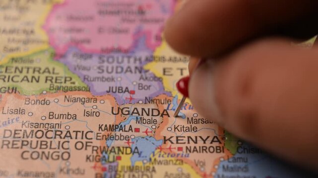 World Map Closeup with Red Pin Marking Uganda Pointed by Hand 4K 60fps