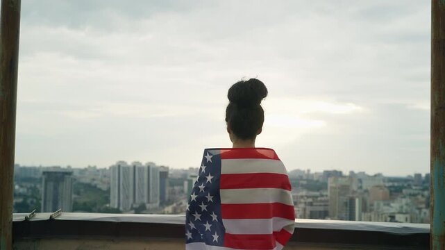 Young Black woman waving American flag on rooftop, proud citizen moment