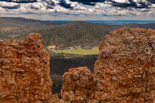 Rocky canyon cliffs frame a vast valley and forested mountains beneath dramatic clouds, capturing a rugged panoramic landscape.