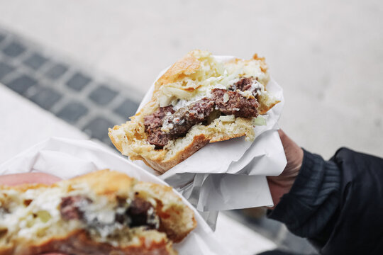 Ćevapi sandwich in hands. Balkan street food with grilled minced meat, onion and cream sauce in bread roll. Traditional cevapcici fast food snack. Close up takeaway meal outdoors