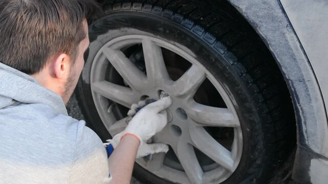 Mechanic tightens lug nut on car wheel. Worker performs automotive maintenance. Technician uses tool for vehicle repair in workshop. Fixing tire for reliability.