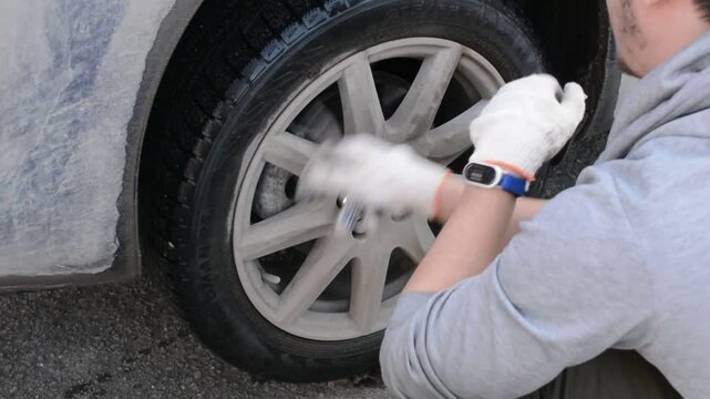 Mechanic man changing car wheel with wrench. Auto service repair process with removing bolt from vehicle tire. Roadside assistance and vehicle maintenance session.