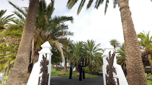 First-person walking through entrance gate into lush palm tree garden of C&eacute;sar Manrique House Museum in Har&iacute;a, Lanzarote, Spain