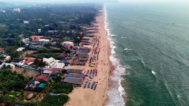 Wide cinematic aerial of a bustling beach featuring patterned sunbeds, scattered beachgoers, and rolling waves. The blend of geometry and natural motion enhances the visual depth.