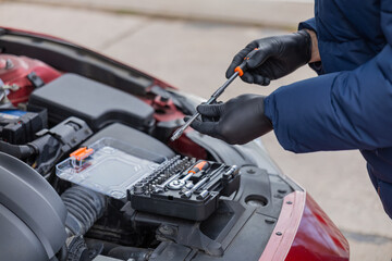 Fototapeta premium Man repairing car engine using tools under open hood during roadside maintenance