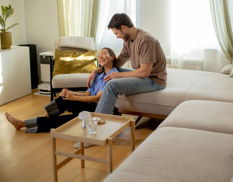 Korean woman sits on floor while Caucasian man sits on couch in bright room