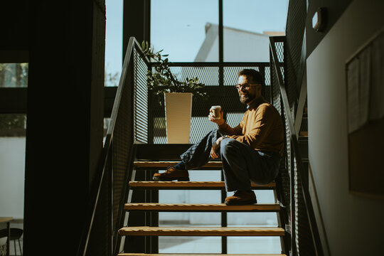 Man sitting on stairs in a cafe holding a drink during the daytime